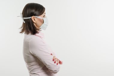 A woman with a mask on to protect her from the coronavirus stands with her arms crossed, reluctant to go to work.