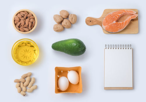 Keto friendly food sit next to a notepad including fish, nuts, avacado, eggs, and more.