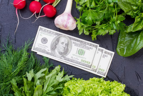 Fresh vegetables lie on a table next to some $100 bills.