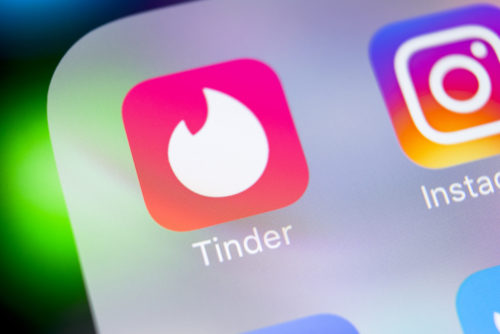 A closeup of a smartphone displaying the Tinder app icon.