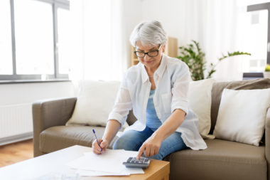 An elderly woman calculating her annuity with a calculator on her couch.