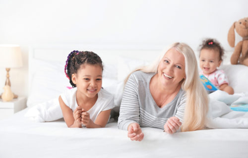 A nanny laying on the bed helping two children.