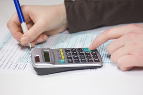 A close up of a person filing their taxes, using a calculator to determine their standard deduction.