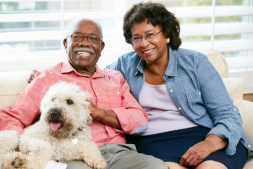 A retired couple sitting on their couch with their dog.