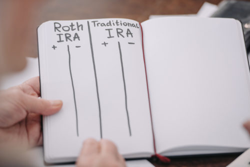 A man holds a notebook weighing the pros and cons of a traditional and Roth IRA.