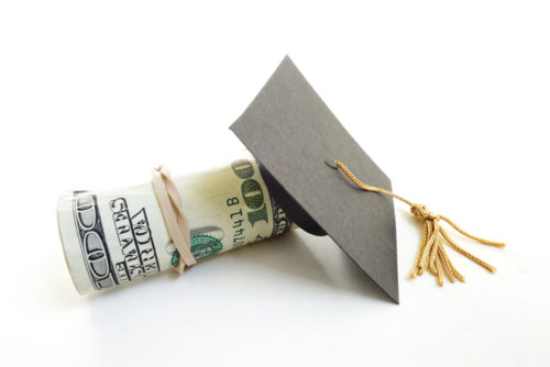 A graduation cap sits on top of a roll on $100 bills, symbolizing student loan payment.