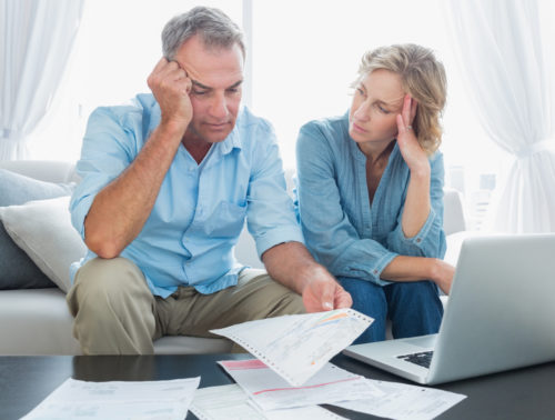 A somber couple going over their bills, trying to decide between debt management or debt settlement.