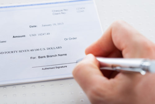 A closeup of a hand preparing to sign a check.