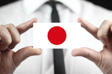 A businessman holds a business card that displays the Japanese flag.