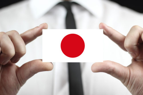 A businessman holds a business card that displays the Japanese flag.