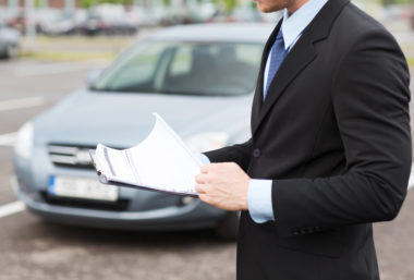 A car salesman looks over documents at a car lot.