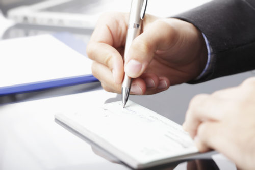 A man's hand filling out a check.