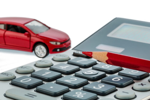A car sits in the background behind a red pen and a calculator that are used to calculate the standard mileage rate of the car.