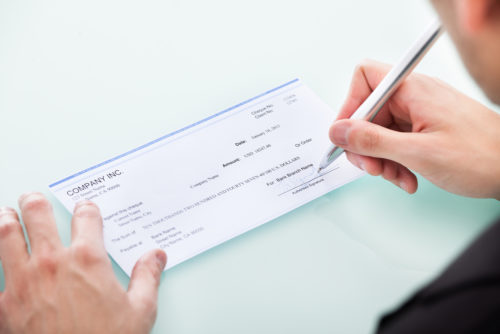 A closeup of a man's hand signing a check.