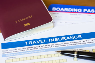 A passport, boarding pass, and pen sit next to a travel insurance form.