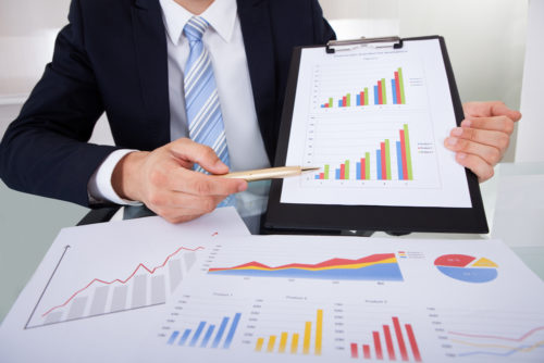 A business analyst with several graphs in front of him points at one with a pen to show the success of a company.