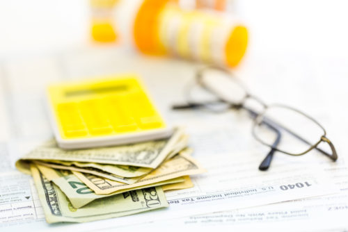 Glasses, cash, calculator, and medicine sit on top of a tax form.