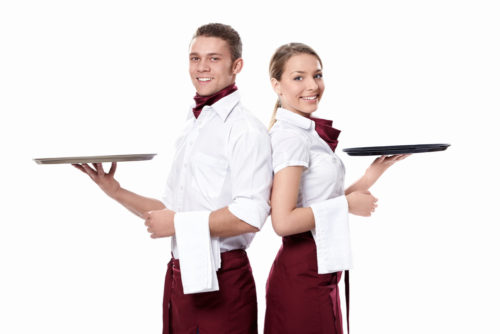 A waiter and waitress standing back to back, holding trays in one hand.