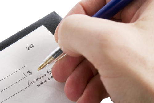 A close up of a hand holding a pen, writing in the amount of a check.