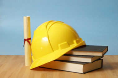 A hard hat sits on top of some trade school textbooks and alongside a certification.