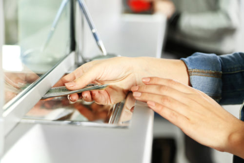 A woman handing cash through a bank teller's window.