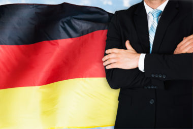 A business standing with his arms crossed in front of the German flag.