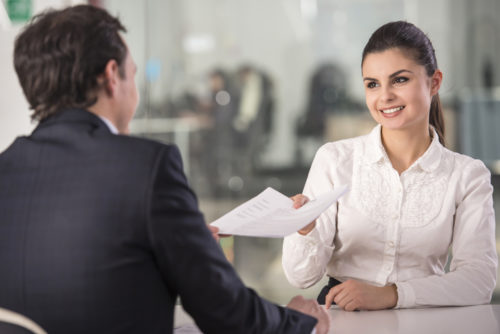 A woman handing over documents to her job interviewer.