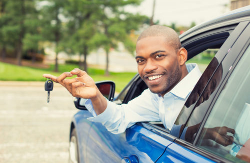 A student leaning out the window of his new car, holding the keys on his finger after just signing a car loan.