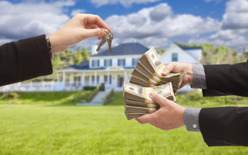 A man holds out stacks of cash while a woman holds out keys in front of a house.