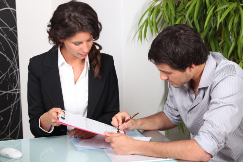 A bank representative holding a document for her client to sign.