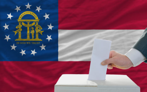 A man putting a ballot in a box in front of the Georgia state flag.