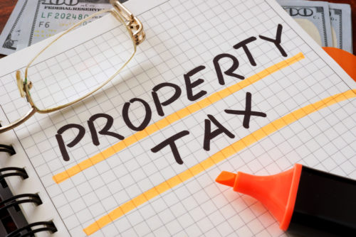 The words "property tax" are underlined with highlighter in a notebook that sits next to eyeglasses and a couple $100 bills.