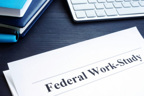 A document titled "federal work-study" lies on a table along with some books and a computer keyboard.