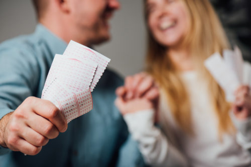 A couple laughing and holding hands while the man holds lottery tickets.