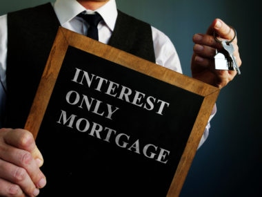 A man holding a set of house keys and a board that reads "interest only mortgage."