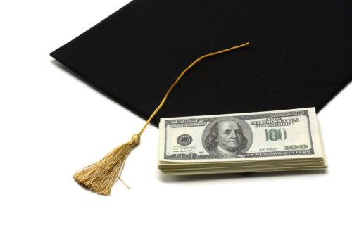 A graduation cap sits under a stack of money.