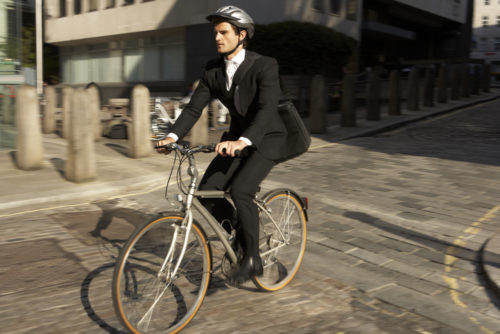 A man dressed in a business suite, bicycling to work with a helmet on.