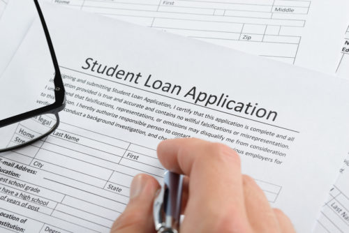 A hand holding a pen over a student loan application.