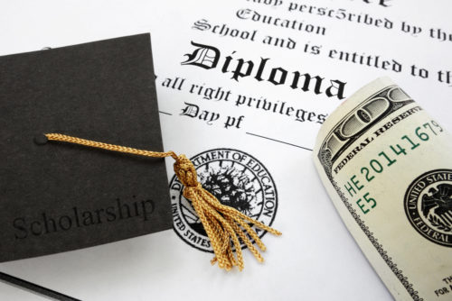A diploma sits under a graduation cap and some cash.