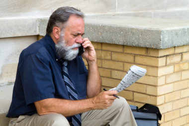 An unemployed man speaking on the phone while holding the newspaper and a pen.