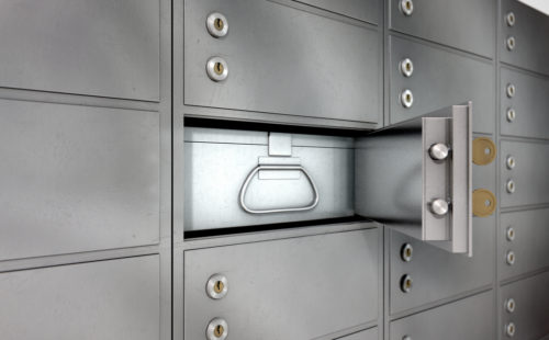 One open safety deposit box on a wall of lockboxes.