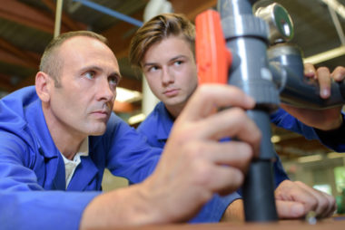 A professor and student working on piping at a trade school.