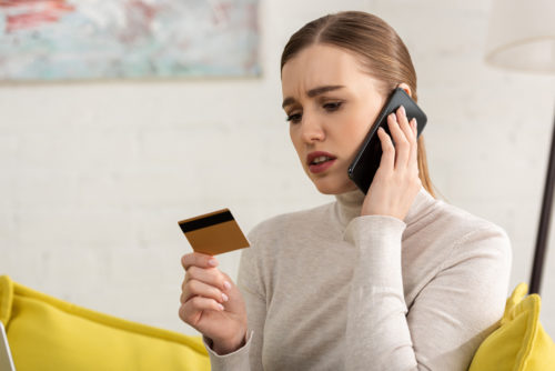 An upset woman holding her credit card while talking on the phone.