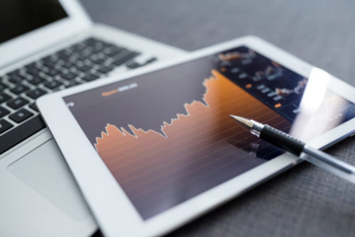 A pen lays on top of a tablet, whose screen displays a chart of economic figures.