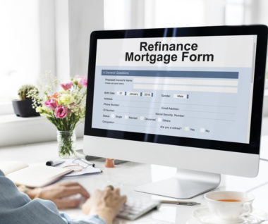 A woman sitting at a computer, whose screen displays a mortgage refinance form.