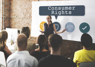 A woman speaking to an audience in front of a screen that reads "consumer rights."