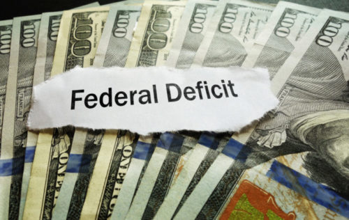 A torn label that reads "federal deficit" sits on top of fanned out $100 bills.
