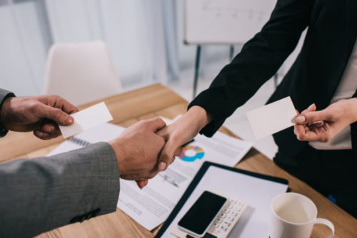 An investing agent shakes hands with a client over a desk with financial graphs on it.