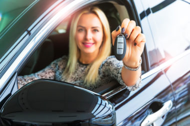 A woman in the driver's seat of a car, holding the keys out the window.