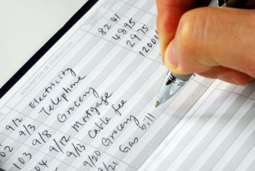 A close up of a man's hand balancing his checkbook.